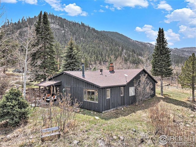 back of property featuring a chimney, a mountain view, a wooded view, and roof with shingles