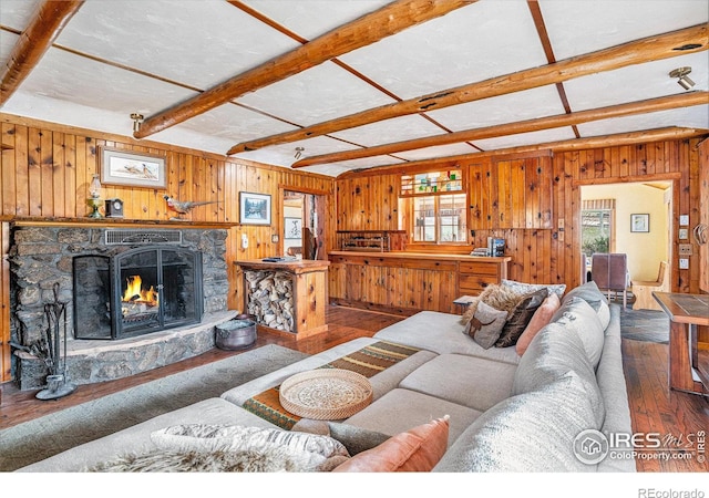 living area featuring wood-type flooring, wooden walls, beam ceiling, and a stone fireplace