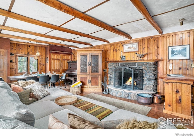 living room featuring wood finished floors, wooden walls, beam ceiling, and a stone fireplace