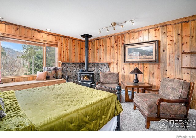 bedroom featuring a wood stove, wooden walls, and carpet flooring