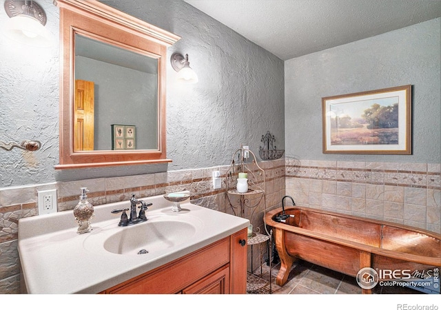 bathroom featuring tile walls, a textured wall, vanity, a freestanding bath, and tile patterned flooring