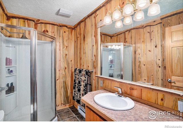 bathroom with a shower stall, wooden walls, a baseboard radiator, a textured ceiling, and vanity