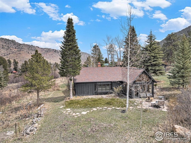 view of front facade featuring a mountain view, a chimney, a front lawn, and a patio area