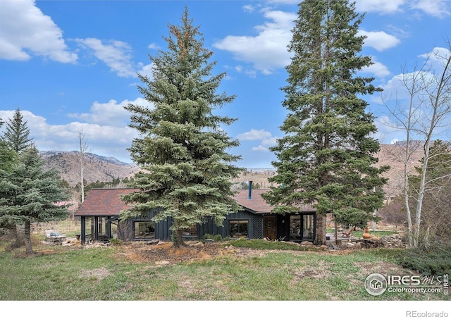 view of property hidden behind natural elements featuring board and batten siding, a mountain view, and a front yard