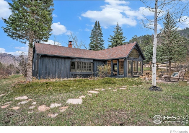 view of front of house featuring board and batten siding, a chimney, a front yard, a shingled roof, and a patio