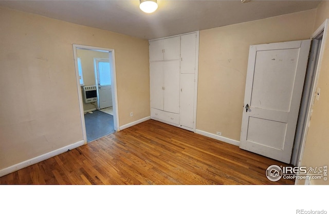401 Park St, Sterling, CO 80751 - unfurnished bedroom featuring heating unit, baseboards, a closet, and wood finished floors