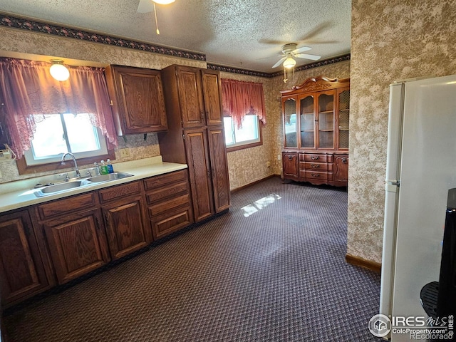 kitchen with a ceiling fan, a textured ceiling, a sink, freestanding refrigerator, and wallpapered walls