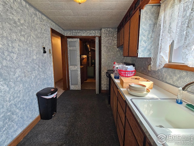 kitchen featuring brown cabinets, a sink, light countertops, dark colored carpet, and wallpapered walls