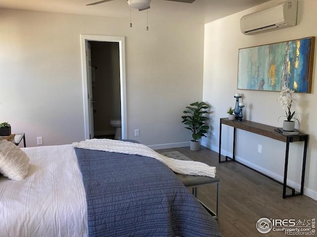 bedroom with baseboards, a wall unit AC, wood finished floors, and ensuite bath