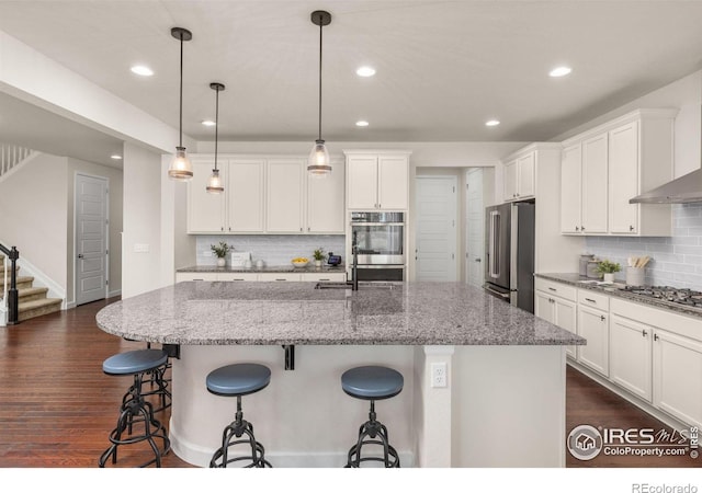 5845 Shadow Creek Ct, Windsor, CO 80528 - kitchen with appliances with stainless steel finishes, backsplash, white cabinets, a kitchen island with sink, and a kitchen breakfast bar