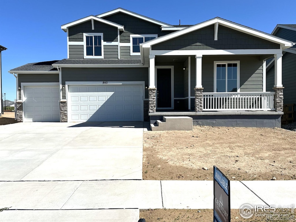 craftsman-style house featuring an attached garage, a porch, driveway, and stone siding