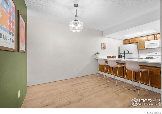 kitchen with white appliances, light countertops, hanging light fixtures, and light wood-type flooring