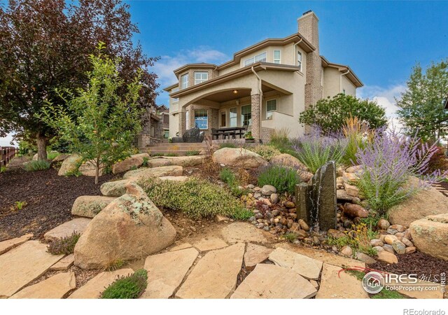 back of property with stucco siding, covered porch, and a chimney