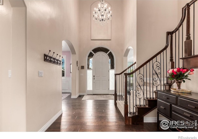 entryway with arched walkways, a high ceiling, baseboards, and dark wood-style flooring