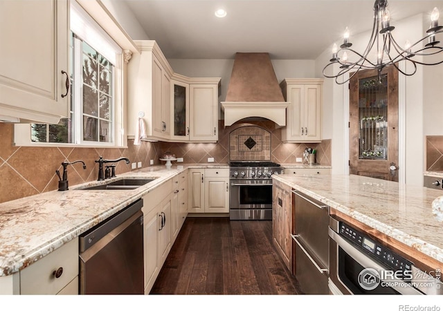 kitchen with dark wood-style flooring, appliances with stainless steel finishes, cream cabinets, a sink, and custom range hood