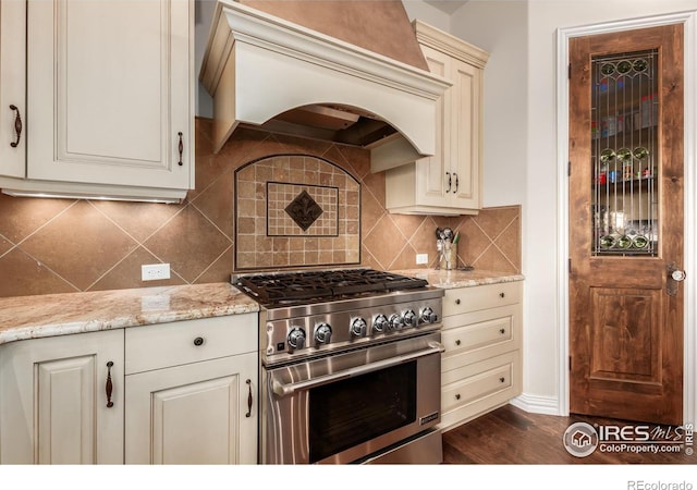 kitchen featuring dark wood-style flooring, high end stove, tasteful backsplash, light stone countertops, and premium range hood