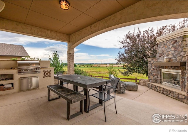 view of patio featuring an outdoor stone fireplace, outdoor dining area, and area for grilling