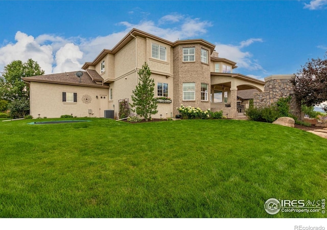 rear view of property with central air condition unit, stucco siding, and a yard