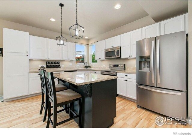 3803 Peach St, Wellington, CO 80549 - kitchen with appliances with stainless steel finishes, a kitchen island, white cabinets, light wood finished floors, and recessed lighting