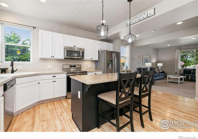3803 Peach St, Wellington, CO 80549 - kitchen featuring appliances with stainless steel finishes, a sink, light wood finished floors, white cabinets, and a kitchen island