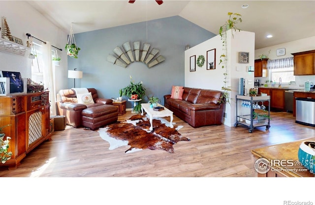living room with a ceiling fan, light wood finished floors, and vaulted ceiling