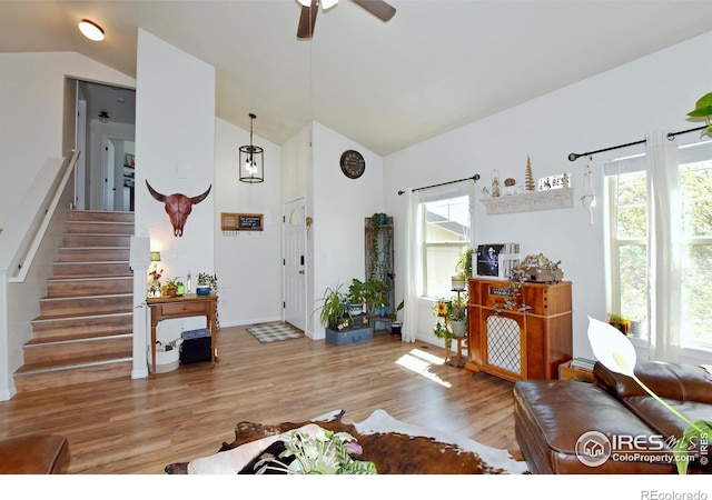 living room with plenty of natural light, ceiling fan, wood finished floors, high vaulted ceiling, and stairs