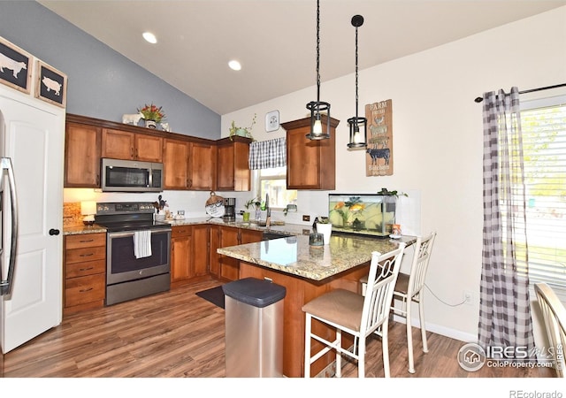 kitchen with light wood finished floors, brown cabinetry, stainless steel appliances, a peninsula, and vaulted ceiling