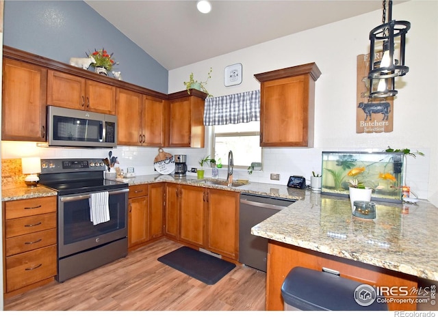 kitchen with backsplash, appliances with stainless steel finishes, brown cabinets, a sink, and light wood-style floors