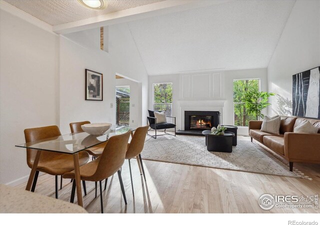 dining space with wood finished floors, a wealth of natural light, a fireplace, and beamed ceiling