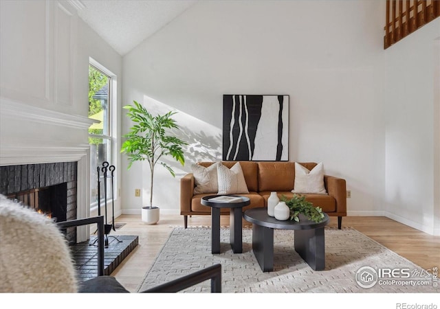 living area with baseboards, light wood-style flooring, vaulted ceiling, and a fireplace
