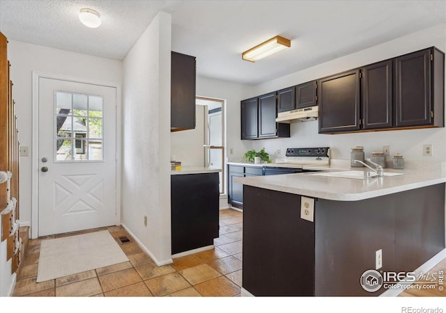 kitchen with a sink, light countertops, range, freestanding refrigerator, and under cabinet range hood