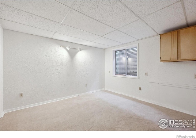 finished below grade area with baseboards, a textured wall, a paneled ceiling, and carpet
