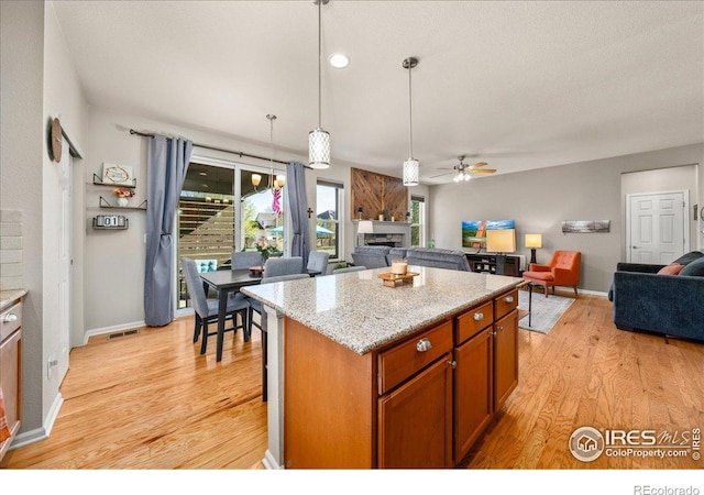 kitchen featuring visible vents, a fireplace, ceiling fan, open floor plan, and light wood-style floors