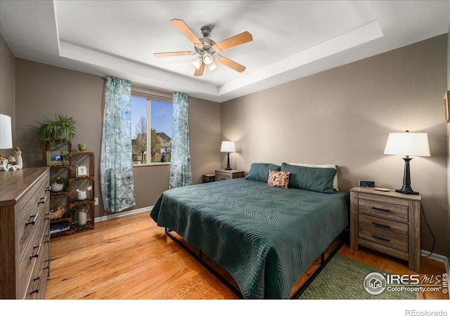 bedroom featuring a tray ceiling, a ceiling fan, light wood-style flooring, and baseboards