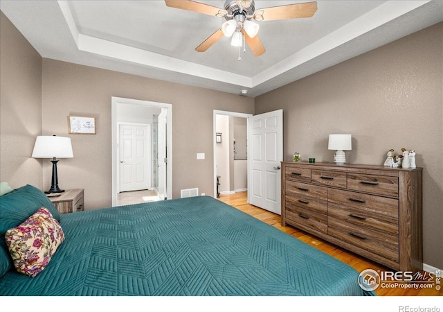 bedroom featuring light wood-style floors, visible vents, a raised ceiling, and ceiling fan