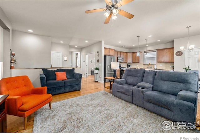 living room featuring recessed lighting, light wood-type flooring, and ceiling fan with notable chandelier