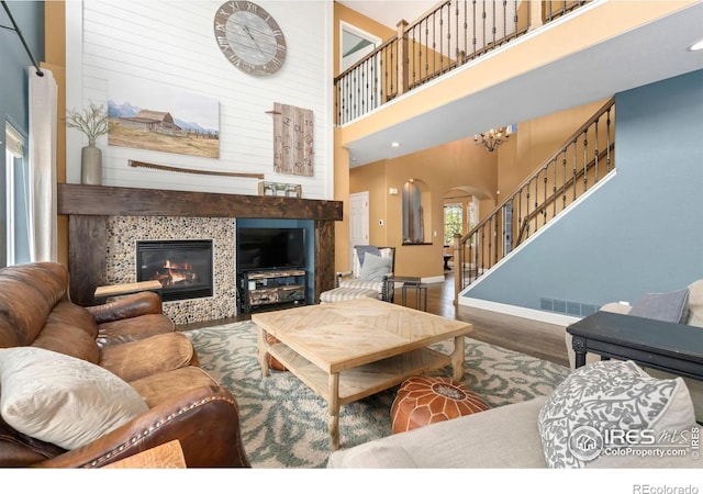 living area featuring a towering ceiling, visible vents, arched walkways, wood finished floors, and baseboards