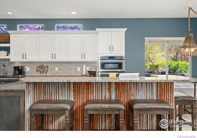 kitchen with decorative backsplash, a breakfast bar area, stainless steel double oven, and white cabinets