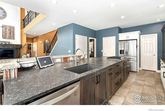 kitchen with a sink, dark stone counters, light tile patterned flooring, and stainless steel appliances