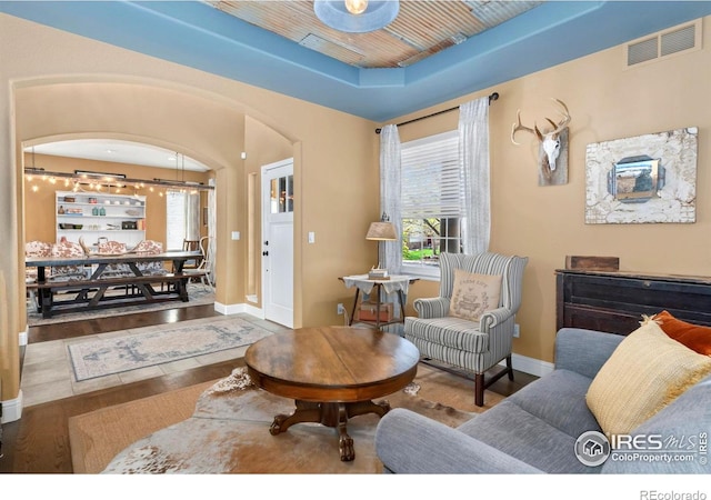 living room with visible vents, wood finished floors, baseboards, a raised ceiling, and arched walkways