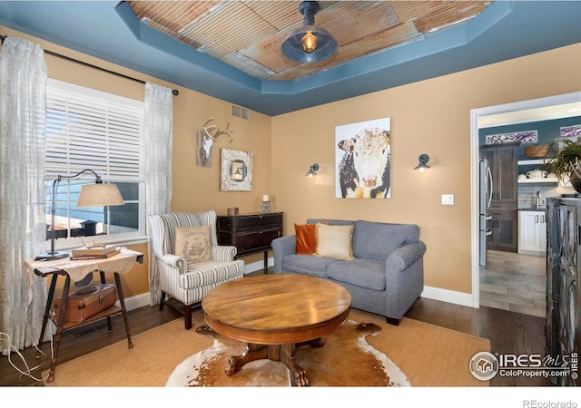 living area featuring a tray ceiling, visible vents, baseboards, and wood finished floors