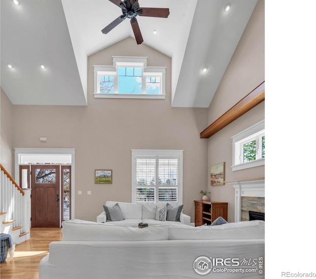 living area with ceiling fan, a fireplace, high vaulted ceiling, stairs, and wood finished floors