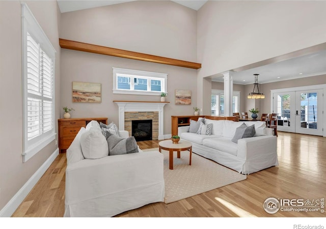 living room with a stone fireplace, french doors, ornate columns, and light wood-style flooring