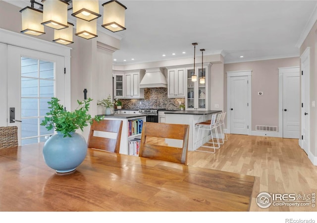 kitchen with visible vents, glass insert cabinets, premium range hood, stainless steel gas range, and tasteful backsplash