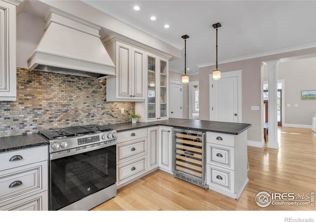kitchen with stainless steel range with gas stovetop, a peninsula, wine cooler, custom range hood, and ornate columns