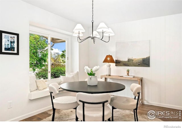 dining area with baseboards, wood walls, wood finished floors, and a notable chandelier