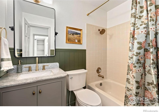 bathroom with vanity, shower / tub combo with curtain, a wainscoted wall, and toilet