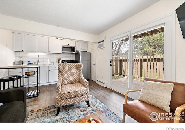 living room with a wall unit AC, wood finished floors, and baseboard heating