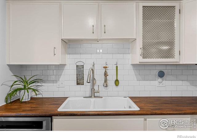 kitchen with white cabinets, wood counters, a sink, and tasteful backsplash