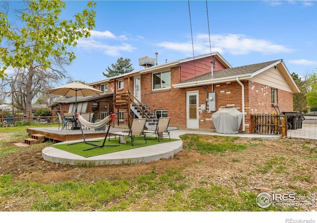 back of property featuring brick siding, a patio area, a wooden deck, and fence